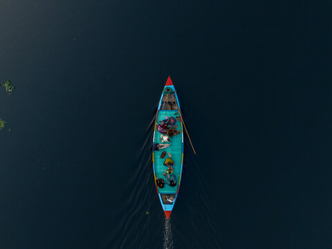 Aerial view of a vibrant turquoise boat cuts through the dark waters, its red and blue accents popping against the somber backdrop, Dhaka, Dhaka Division, Bangladesh.