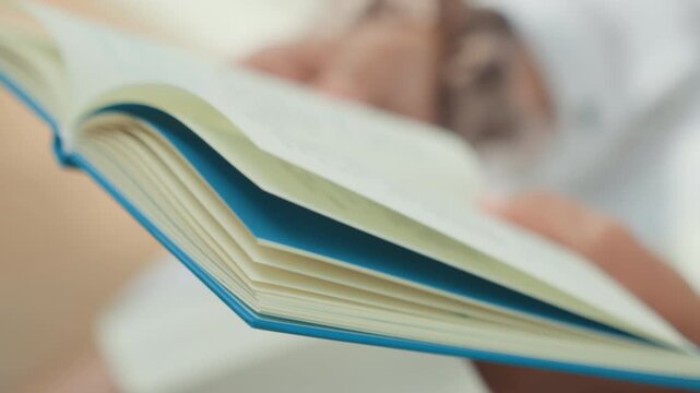 Closeup hands holding open journal, caucasian writer in soft indoor light turning pages slowly, textured paper and blue cover in focus, cozy quiet mood for study and note revising