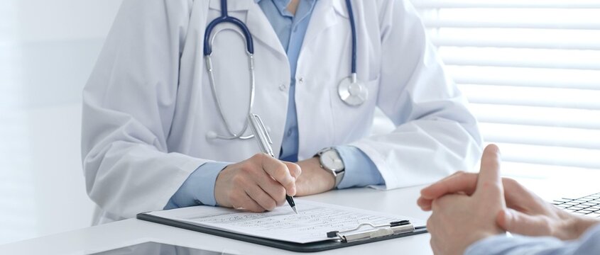 Female medical professional filling prescription, advising patient on health issues during clinical consultation. Medicine and healthcare concept