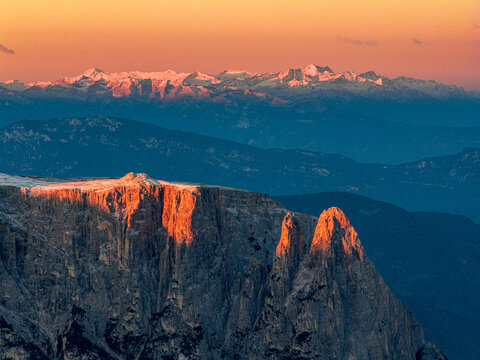 Aerial view of Sciliar peaks kissed by the warm glow of the rising sun, contrasting sharply with the cool blues of the Alps mountains, Seiser Alm, Bolzano, South Tyrol, Italy.
