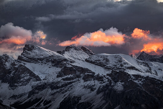 Aerial view of snow-capped mountains pierce the twilight sky, clouds ablaze with fiery hues, casting long shadows across the alpine landscape, South-Tyrol, Trentino-Alto Adige, Italy.