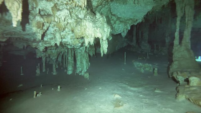 A cave diver moves close to limestone columns inside a submerged cavern system with clear water in Cenote Dos Ojos