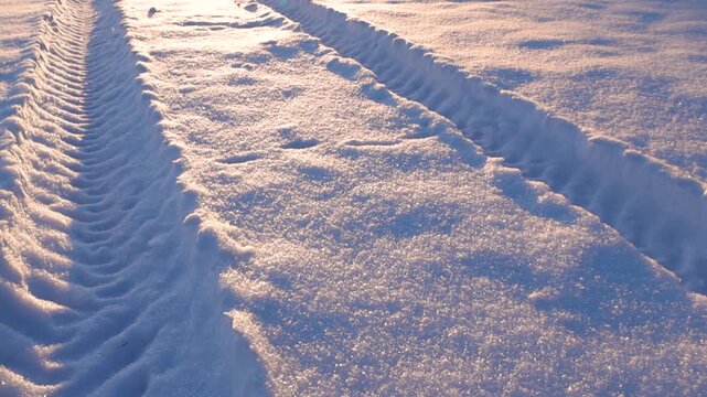 Tractor tire tracks in fresh winter snow during sunset