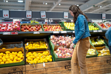 Obraz premium Young woman choosing fresh produce in a supermarket during daily grocery shopping