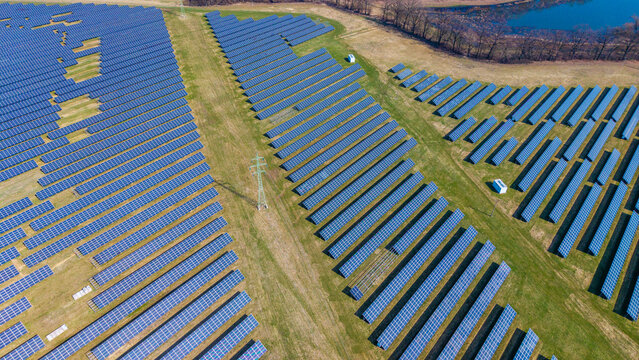 Aerial view of vast solar arrays stretching across the landscape under a clear sky, contrasting with patches of green and brown fields, Sevetin, South Bohemian Region, Czechia.