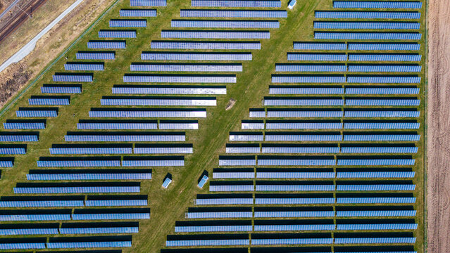 Aerial view of neatly organized solar panels reflecting the sky amid green grass and brown fields, creating a geometric contrast, Sevetin, South Bohemian Region, Czechia.