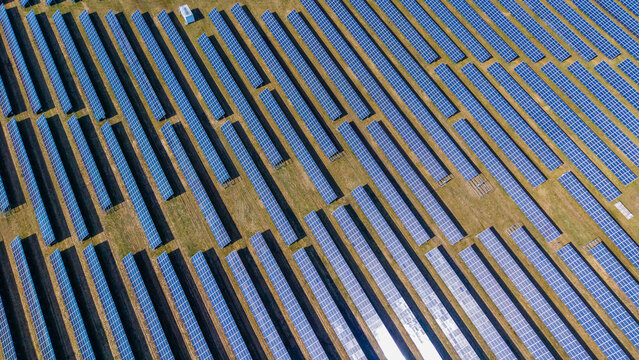 Aerial view of neatly arrayed solar panels gleam under the sun, creating a striking geometric pattern against the golden grass, Sevetin, South Bohemian Region, Czechia.