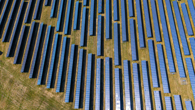 Aerial view of solar panels arrayed in geometric patterns across the landscape, reflecting the bright sky above, Sevetin, South Bohemian Region, Czechia.