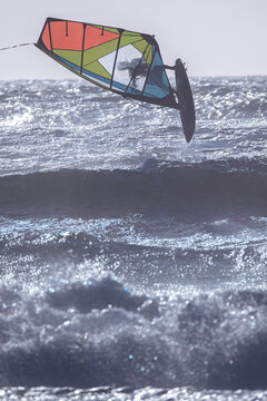 Cascais, Portugal - 28 March 2026: View of a windsurfer silhouetted against massive crashing waves at Praia do Guincho with white sea foam and deep blue water.