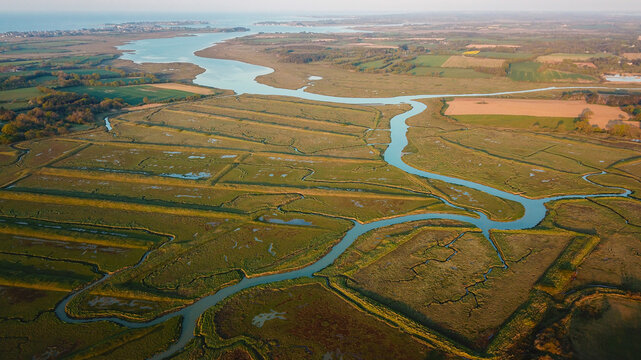 Aerial view of waterways carving through the cultivated landscape, reflecting the sky's soft light in Ambon, Brittany, France.