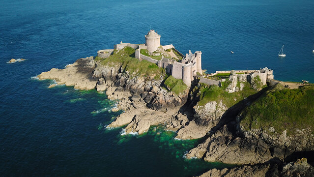 Aerial view of the rugged, rocky coastline topped by the imposing Fort la Latte, a medieval fortress bathed in golden sunlight, Plevenon, Bretagne, France.