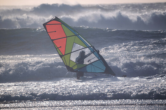 Cascais, Portugal - 28 March 2026: View of a windsurfer silhouetted against massive crashing waves at Praia do Guincho with white sea foam and deep blue water.