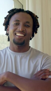 Vertical video: Glancing at camera causing man turning smiling folding arms in apt wearing gray tee
