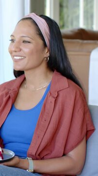 Vertical video: Listening woman in rust shirt replying to offscreen voice on sofa, holding plate