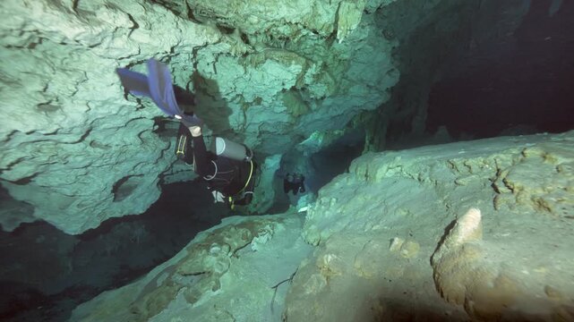 Diver swims above sandy cave floor illuminating rock formations and sediment in Cenote Dos Ojos, Quintana Roo, Mexico
