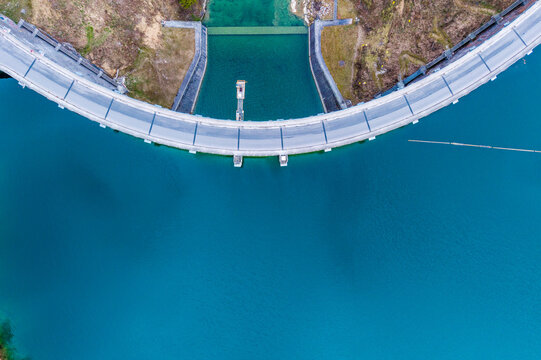 Aerial view of the Klaus Dam curving gracefully over the turquoise waters, a stark contrast to the rugged, brown landscape, Klaus an der Pyhrnbahn, Oberosterreich, Austria.