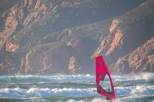 Cascais, Portugal - 28 March 2026: View of a windsurfer silhouetted against massive crashing waves at Praia do Guincho with white sea foam and deep blue water.