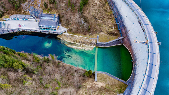 Aerial view of the Klaus dam curving against the turquoise water, a stark contrast to the surrounding brown, Klaus an der Pyhrnbahn, Oberosterreich, Austria.