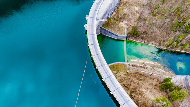 Aerial view of the Staudamm Klaus dam holding back the turquoise water contrasting with the earthy tones of the surrounding landscape, Klaus an der Pyhrnbahn, Oberosterreich, Austria.