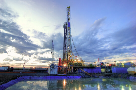 Onshore drilling rig at dusk, mud pit in the foreground