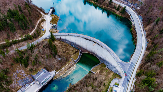 Aerial view of the imposing Staudamm Klaus dam, its concrete curve holding back the turquoise waters reflecting the sky, bordered by dense forests, Klaus an der Pyhrnbahn, Oberosterreich, Austria.