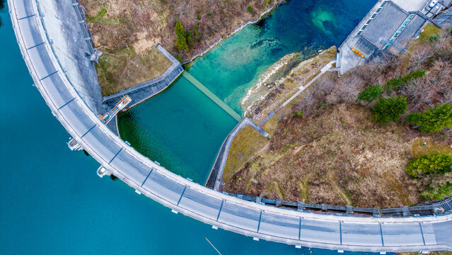 Aerial view of the stark concrete dam curving against the turquoise waters, a testament to engineering amidst the natural landscape, Klaus an der Pyhrnbahn, Oberosterreich, Austria.