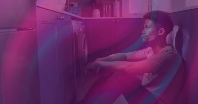 Man sitting on floor waiting for washing machine cycle, magenta teal bands sweeping overlaying man