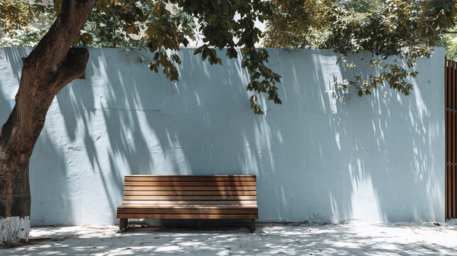 Empty wooden bench in front of blue wall with tree shadows