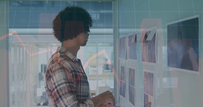 Designer approaching wall, studying top row, adjusting sticky notes and aligning prints for layout