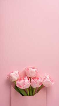Happy Mother's Day vertical greeting with pink tulip bouquet tucked in an envelope on pastel background