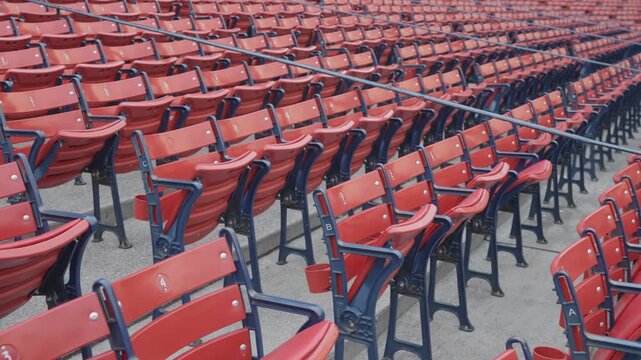 Rows of empty red stadium seats with navy blue metal frames arranged in sections at a baseball park or sports venue.