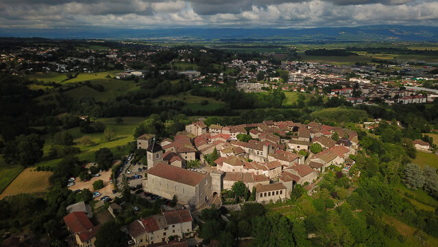 Aerial view of rustic rooftops cluster tightly in the ancient village, a timeless scene of warmth against a backdrop of rolling green hills, Perouges, Auvergne-Rhone-Alpes, France.