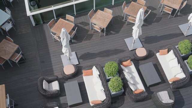 Aerial view of a luxurious outdoor patio deck featuring wicker lounge sofas, wooden dining tables, closed umbrellas, and green planters overlooking a manicured golf course.