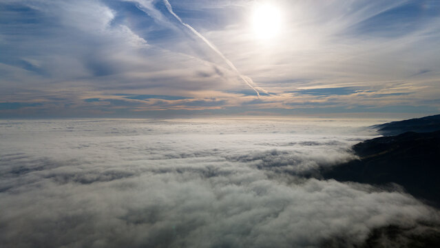 Aerial view of a sea of clouds rolling over the dark hills under a bright sun and blue sky, Malibu, California, United States.