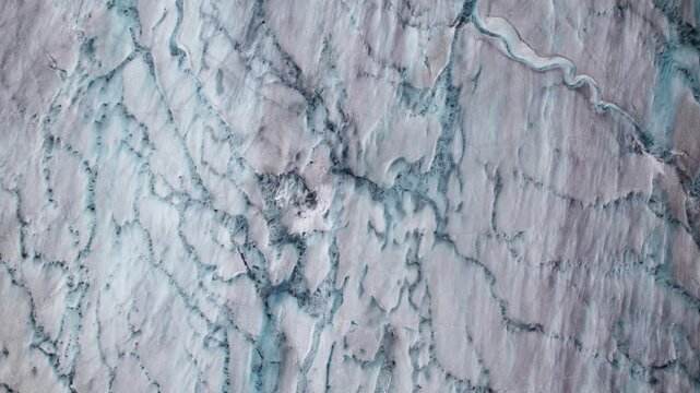 Vertical 4k drone view of the Aletsch Glacier surface showing crevasse networks, melt channels, and fractured ice patterns formed by stress, flow dynamics, and seasonal melting in the Swiss Alps