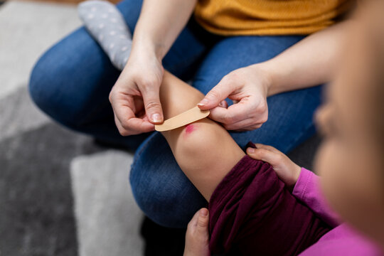 Mother applying adhesive bandage on little girl's scraped knee at home