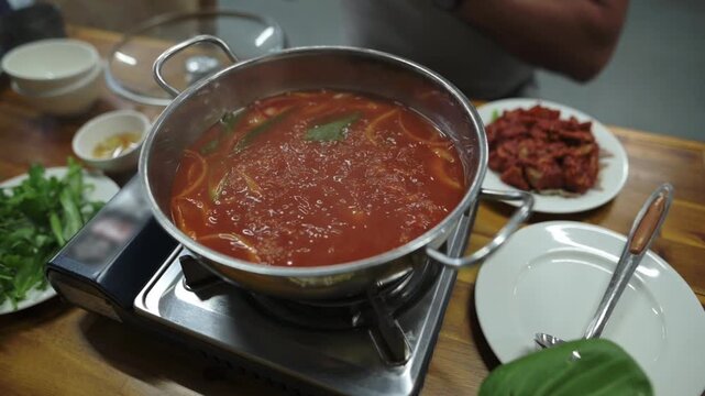 Spicy Boiling Soup. Tasty Hotpot With Fragrant Herbs. Vivid Red Simmering Pot With Aromatic Bay Leaves. Seething Hotpot Bubbles As Fragrant Bay Leaves Drift Upwards In Restaurant Atmosphere