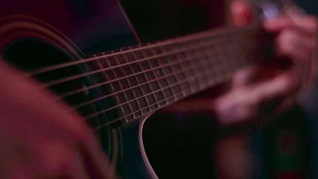 Warm-toned close-up of an acoustic guitar being strummed, with shallow depth of field highlighting strings and fretboard. Rhythmic hand movement creates an intimate, cinematic musical moment. Close-up