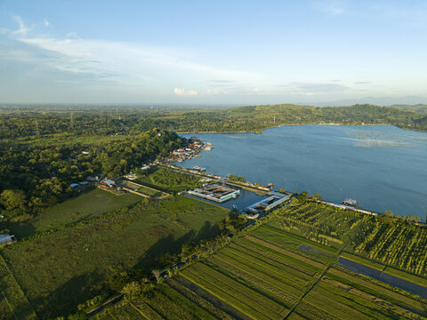 Aerial view of the serene Rawa Jombor lake, where the tranquil blue waters meet the vibrant green fields, Klaten Regency, Jawa Tengah, Indonesia.