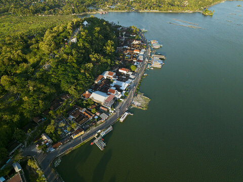 Aerial view of lush greenery meeting the tranquil waters, homes nestled along the shore, a vibrant tapestry of nature and dwellings, Klaten Regency, Jawa Tengah, Indonesia.