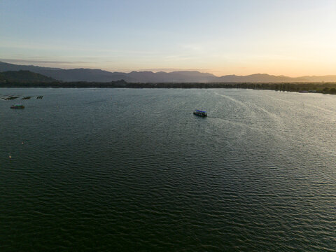 Aerial view of a tranquil expanse of water reflecting the soft hues of the sky, with distant mountains and boats adding depth to the scene, Klaten Regency, Jawa Tengah, Indonesia.