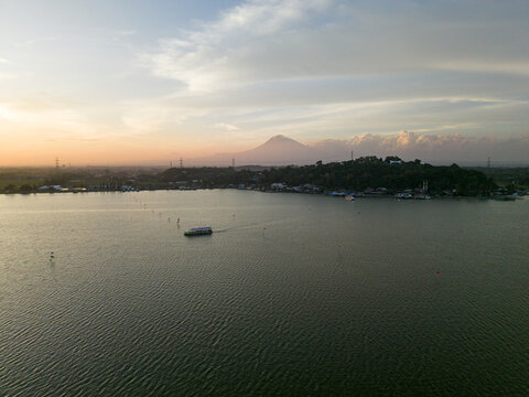 Aerial view of the tranquil lake mirroring the soft sunset hues, with the distant mountain providing a stunning backdrop, Klaten Regency, Jawa Tengah, Indonesia.