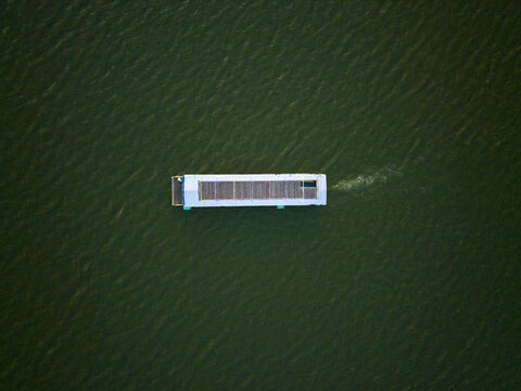Aerial view of a boat gliding across the still, dark waters of Rawa Jombor, its wake a subtle contrast to the surrounding expanse, Klaten, Jawa Tengah, Indonesia.