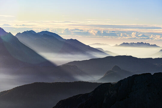 Aerial view of majestic mountains rise through layers of mist, their peaks kissed by the soft light of dawn, Dolomites of region Friuli as seen from Veneto, Italy.