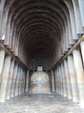 Interior view of the ancient Buddhist rock-cut Chaityagriha prayer hall with a monolithic Stupa and wooden ribbed ceiling at Bhaja Caves, India.