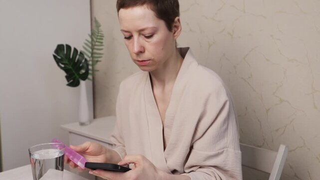 cancer patient uses smartphone with pillbox and water, tracking medication reminders at home