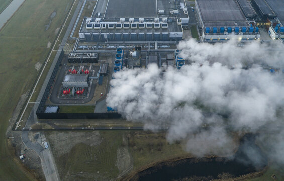 Aerial view of a large data center complex featuring multiple buildings, cooling towers, and steam plumes rising from the industrial facility