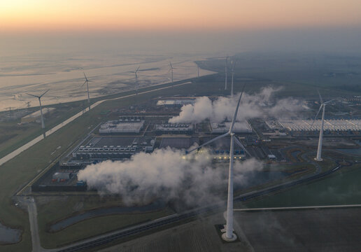 Aerial view of hyperscale data center infrastructure emitting steam from cooling towers, surrounded by wind turbines at eemshaven, netherlands