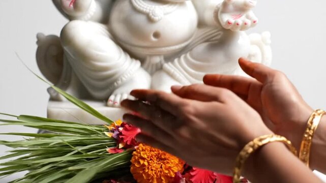 Vinayaka Chaturthi Close-up of a devotee's hands offering fresh green Durva grass and flower petals at the feet of a marble Ganesha statue