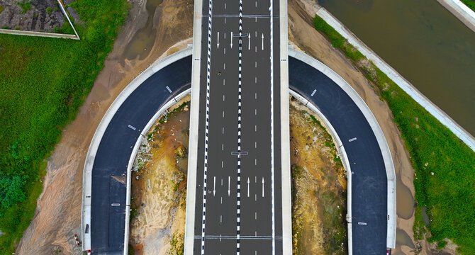 Aerial view of a sleek, modern highway interchange with sharp black asphalt contrasting with surrounding green vegetation, Ikeja, Lagos, Nigeria.